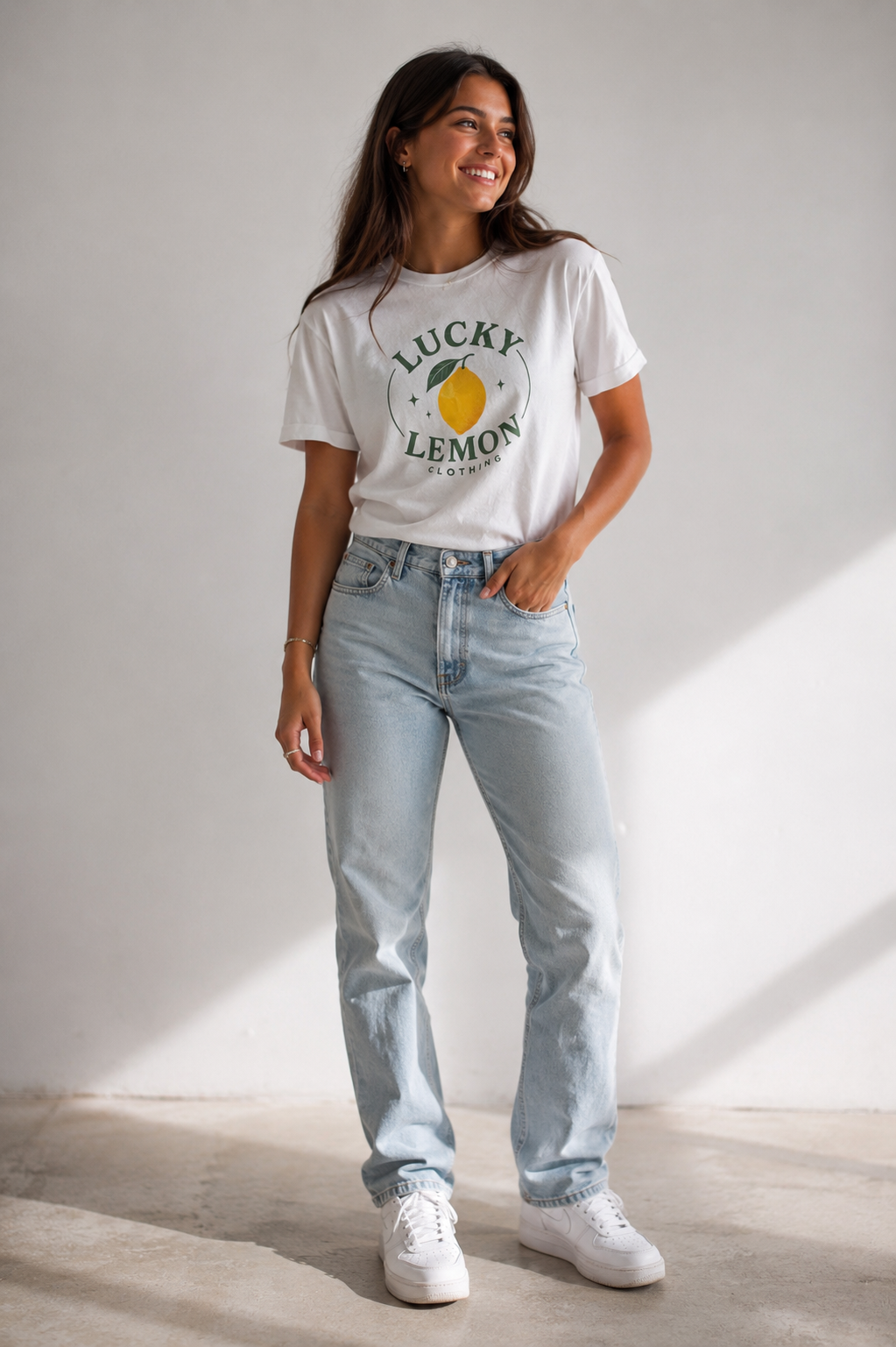 Woman wearing the white Lucky Lemon Clothing tee with the lemon badge print at the top left and a matching back logo, with light-wash jeans